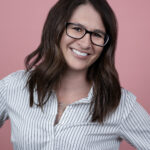 woman with brown hair and glasses wearing a blue pinstripe shirt.